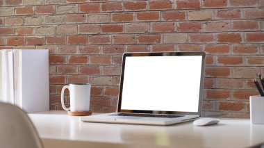 Rahat bir ofis. Dizüstü bilgisayar, kırtasiye ve saksı bitkisi beyaz masada..