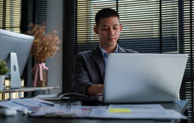 Yakışıklı genç işadamı modern ofiste otururken bilgisayar kullanıyor..