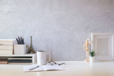 Bright modern workplace with flower pot, coffee cup, picture frame and books on white table. Copy space for your text.