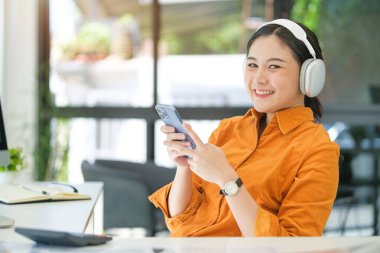 Kablosuz kulaklık takan güzel genç bir kadın modern ofiste cep telefonu kullanıyor..