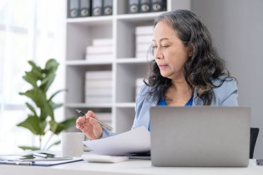 Evrak işleri hakkında bilgi okuyan ve masa başında çalışan yaşlı bir iş kadını..