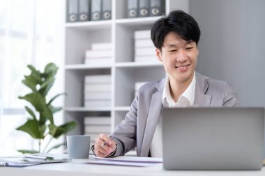 Çağdaş ofiste dizüstü bilgisayarda çalışan yakışıklı Asyalı genç adam..