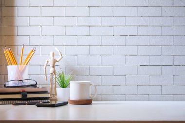 Beyaz masa üzerinde kahve, kitap, çiçek ve kalem tutacağı olan şık bir çalışma alanı..