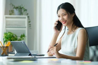 Genç Asyalı kadın cep telefonuyla konuşuyor ve dışarıda dizüstü bilgisayarla çalışıyor..