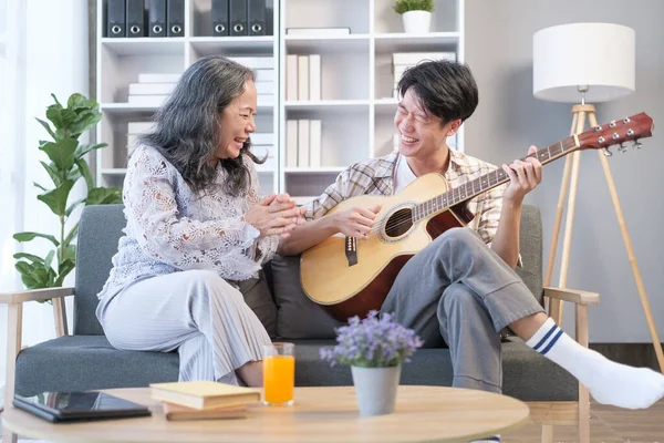 Happy family. Happy smiling teenage  man singing and playing guitar with grandmother, enjoying leisure time together,