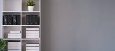 Beyaz kitaplık ve gri duvarda beyaz bir poster. Metnin için boşluk kopyala.