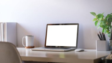 Rahat bir ofis. Dizüstü bilgisayar, kırtasiye ve saksı bitkisi beyaz masada..