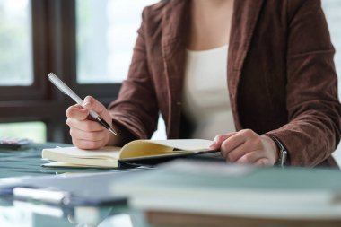 İş kadınının önemli notlar yazarken, iş yerinde otururken plan yaparken görüntüsü kesilmiş..