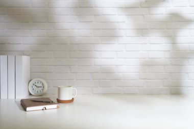 Minimum işyeri, ev bitkisi, defter, bardaklar ve kahve fincanı beyaz masanın üzerinde pencere perdelerinden güneş ışığı geçiyor..
