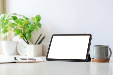 Boş ekranlı dijital tablet, kahve fincanı ve beyaz masadaki saksı bitkisi. Basit işyeri.