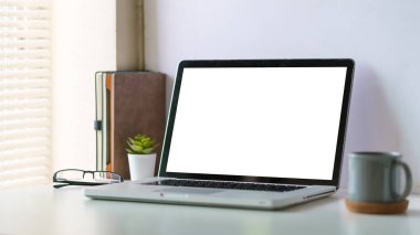 Boş ekranlı dizüstü bilgisayar ve parlak ofis içi beyaz masada bir fincan kahve..