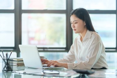 Charming young businesswoman sitting in bright office and working with modern devices.	