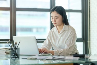 Parlak ofiste dizüstü bilgisayarla çalışan güzel bir iş kadını..