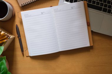 Top view of blank notepad, pen, cup of coffee, houseplant and keyboard on table.