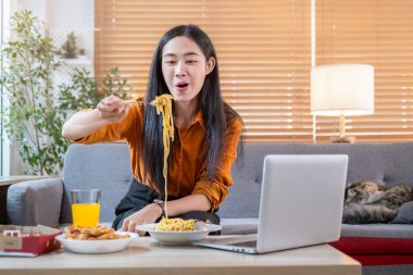 Cheerful young woman sitting on sofa and eating tasty spaghetti. Domestic life and food concept.	