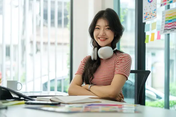 Smiling asian female graphic designer wearing headphone sitting front of computer sat her office.