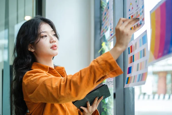 デジタルタブレットを保持し カラーウォッチを見て オフィスでデザインプロジェクトに取り組む若いアジアの女性デザイナー — ストック写真