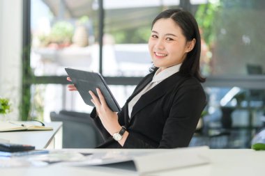 Modern ofiste oturup dijital tablet kullanan çekici genç bir iş kadını..