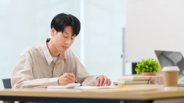 Odaklanmış Asyalı çalışan strateji fikirleri yazıyor, ofis masasında mali raporlar üzerinde çalışıyor..