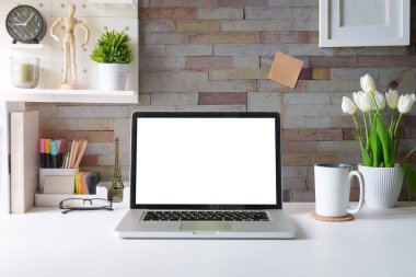 Dizüstü bilgisayar, resim çerçevesi, ev bitkisi ve kırtasiye malzemesi beyaz masada. Modern işyeri.