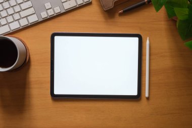 Boş ekranlı dijital tablet, kahve fincanı, kırtasiye ve klavye ahşap masada..
