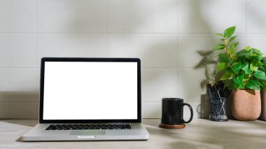 Laptop bilgisayarı, kahve fincanı, beyaz masa üzerinde kalem tutacağı olan minimum iş yeri.