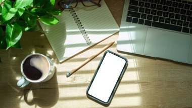 Mockup smart phone, laptop computer, notebook and coffee cup on wood table. Copy space.	