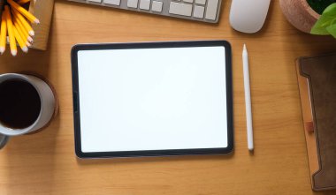 Düz yatış, beyaz ekranlı dijital tabletin üst görüntüsü, kahve fincanı, bardak ve not defteri ahşap çalışma masasında..
