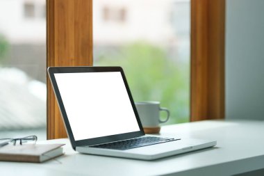 Boş ekranlı dizüstü bilgisayar, ofis masasında bir fincan kahve ve defter..