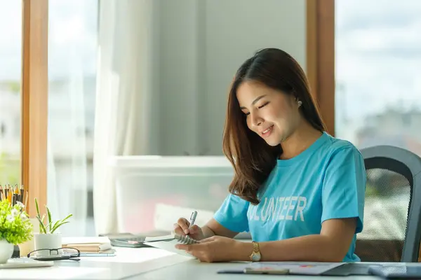 Nice, friendly asian female volunteer wearing volunteer t-shirt working at charity center