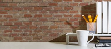 Stylish workplace with books, coffee cup, picture frame and potted plant on white table. Copy space for your text.