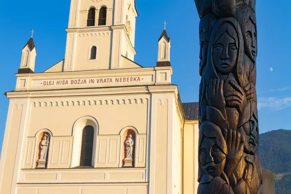 Bohinjska Bistrica, Slovenya - 19 Ağustos 2018: Barok stili Aziz Niklas Kilisesi 'nin ana cephesi ahşap bir totem önündeydi