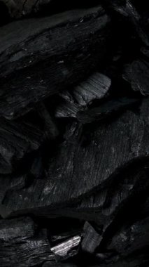 Black background of heap natural charcoal mineral used in industry and food preparation rotate. Vertical. Top view. Close up.