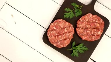 Round fresh raw mince beef burger cutlet ready to prepare rotate on dark kitchen board. Ingredient for hamburger preparation on domestic kitchen. Top view. Close up.