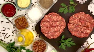 Round fresh raw mince beef burger cutlet with spices and sauce rotate on dark kitchen board. Ingredient for hamburger preparation on domestic kitchen. Top view. Close up.