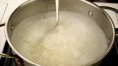 Boiling round rice in metal pot is stirred with spoon to prepare nutritious side dish. Preparation vegan or vegetarian healthy food. Slow motion. Close-up.