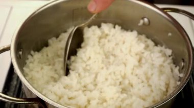 Boiled round rice in metal pot take with kitchen spoon. Preparation vegan or vegetarian healthy food. Slow motion. Close-up.