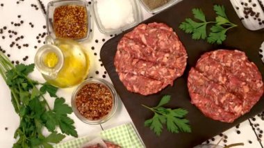 Round fresh raw mince beef burger cutlet with spices and sauce rotate on dark kitchen board. Ingredient for hamburger preparation on domestic kitchen. Top view. Close up.