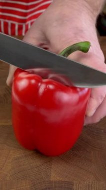 Chef hands slicing sweet bell pepper with sharp knife into pieces on chopping board. Cooking vegetarian or vegan food on domestic kitchen. Vertical. Close up.