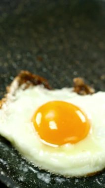 Fried eggs or omelette frying in hot oil in grill pan with nonstick coating. Preparation fast vegetarian food on domestic kitchen. Slow motion. Vertical. Close-up.