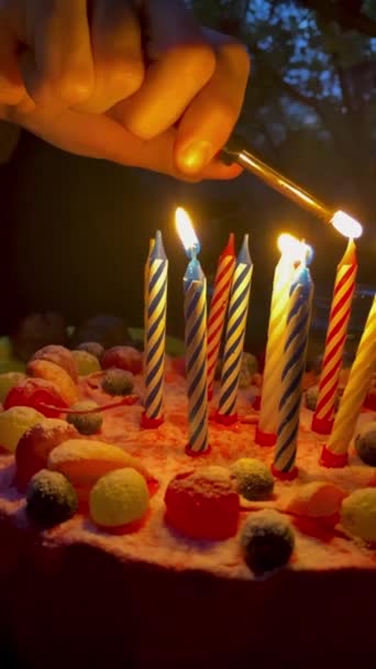 暗闇の中でライターを燃焼する誕生日ケーキの人間の手の照明ろうそく 夏には外でシンボルの誕生日としてろうそくを燃やす 閉じろ — ストック動画