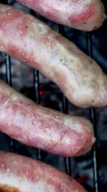 BBC 'de kırmızı domatesle kızartılmış ve maşayla döndürülmüş yağlı domuz sosisi. Hafta sonu hazırlığı için arka bahçede kömür var. Üst Manzara. Dikey. Kapat..