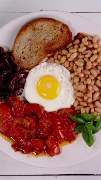 フライドエッグ トマト 豆を使用したベジタリアン向けの伝統的な英語朝食 ヘルシーなタンパク質ベジタリアンブレックファーストとフライドタマネギとパン トップビュー 垂直に 選択的なフォーカス — ストック動画