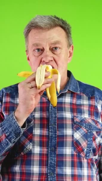 カメラを見ながら健康的な新鮮な黄色いバナナを食べています ビタミンや抗酸化物質を含む健康的なベジタリアンやビーガンダイエット グリーンスクリーン クロマキー バーティカル — ストック動画