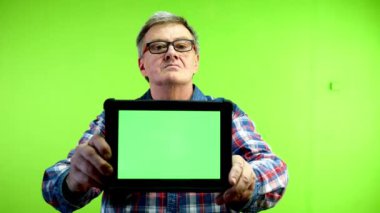 Üst düzey beyaz adam yatay yeşil ekranlı tablet gösteriyor ve gülümsüyor. Reklam veya pazarlama için elinde dijital tablet bulunan kişi. Yeşil ekran, krom anahtar.
