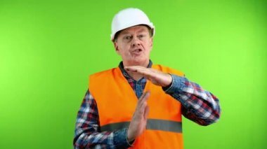 Kıdemli miğferli müteahhit mola sembolü gösteriyor ve herkese jest yapıyor. Olgun inşaatçı işi durdurur ve mola için etrafındaki herkesi toplar. Yeşil ekran. Krom anahtar.