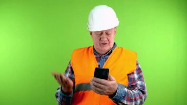 Başlık takmış kıdemli müteahhit telefonda web kamerasıyla iş hakkında konuşuyor. Uzaktan iletişim için teknolojiyi kullanmak, uzaktan konuşmak. Yeşil ekran, krom anahtar.