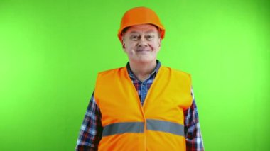 Kıdemli dost canlısı inşaat ustası selamlama ya da veda işareti olarak el sallıyor. Olgun işçi, miğferin kenarına dokunarak ve eliyle selam vererek selam verir. Yeşil ekran, krom anahtar.