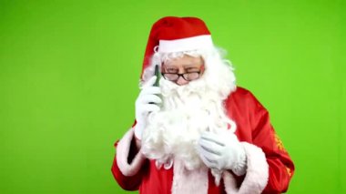 Gözlüklü otantik neşeli Noel Baba akıllı telefonuyla konuşuyor ve el kol hareketi yapıyor. Noel zamanı kırmızı takım elbiseli neşeli Noel Baba. Yeşil ekran. Krom Anahtar.