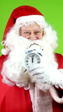 Elinde çalar saat tutan ve saat yüzünü gösteren otantik neşeli Noel Baba. Noel zamanı kırmızı takım elbiseli neşeli Noel Baba. Yeşil ekran. Krom Anahtar. Dikey.